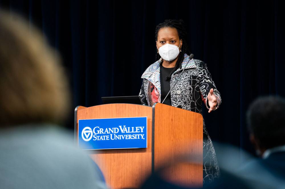 woman behind podium wearing mask speaks to audience